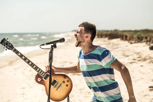 Βράχο στην παραλία, ο μουσικός να παίζει κιθάρα και να τραγουδάει στο μικρόφωνο, η έννοια του ελεύθερου χρόνου και τη δημιουργικότητα — Φωτογραφία Αρχείου