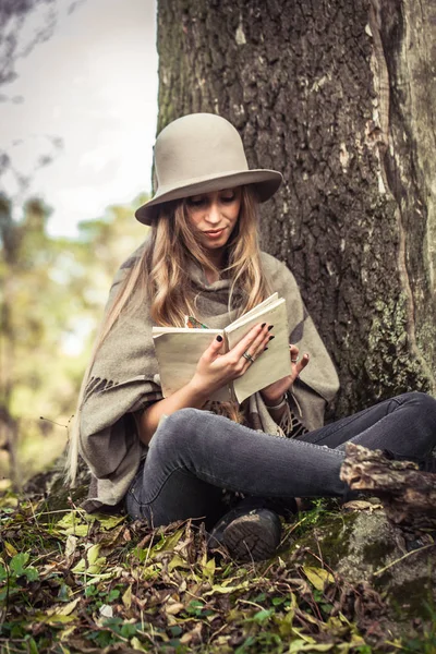 Menina em um chapéu lendo um livro na floresta de outono — Fotografia de Stock