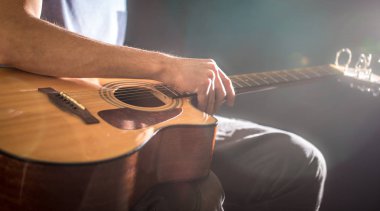 adam oturan bir akustik gitar, yakın çekim, bir ışık, bir