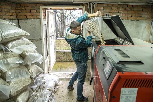 Чоловік завантажує гранули в котел на твердому паливі, економічний h — стокове фото