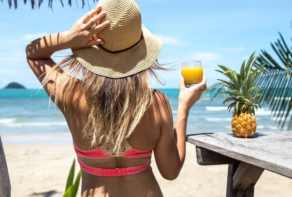 Chica bonita en sombrero de paja y bikini con bebidas de verano en la mano, en medio de las palmeras y la playa — Foto de Stock