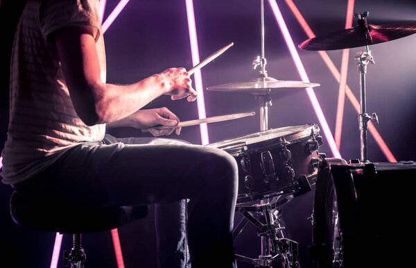 the man plays the drums. Against the background of colored lights and a bright beam of light.