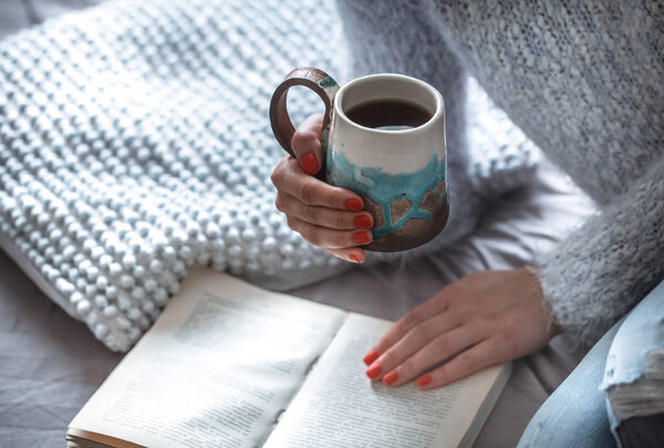 Девушка держит чашку и читает книгу
