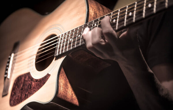 Man playing acoustic guitar on dark background. A musical concep