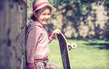 Şık küçük bir kız bir kaykay tutarak ve ou oynarken