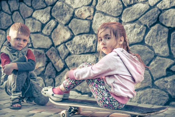Μικρό κορίτσι και αγόρι παίζει για skateboard, ενάντια στο σκηνικό — Φωτογραφία Αρχείου
