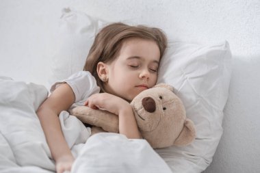 Yumuşak oyuncaklarla yatakta tatlı küçük bir kız.