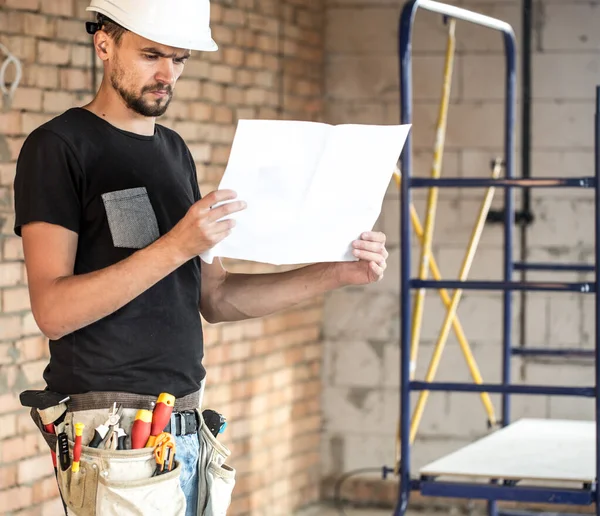 Construtor faz-tudo com ferramentas de construção, olhando para o desenho — Fotografia de Stock