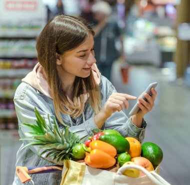 Genç bir kadın süpermarketten içinde telefon olan sebzeler alıyor.