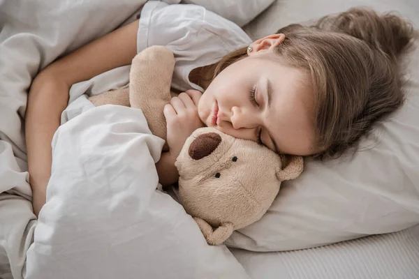Yumuşak oyuncaklarla yatakta tatlı küçük bir kız. — Stok fotoğraf