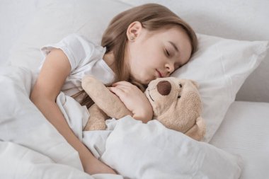 Yumuşak oyuncaklarla yatakta tatlı küçük bir kız.