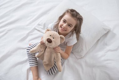 Yumuşak oyuncaklarla yatakta tatlı küçük bir kız.