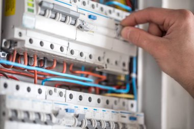 Elektrik santralinde fitillerle çalışan bir elektrik teknisyeni. Elektrik ekipmanlarının kurulumu ve bağlantısı. Kapat..