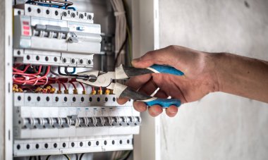 Elektrik santralinde fitillerle çalışan bir elektrik teknisyeni. Elektrik ekipmanlarının kurulumu ve bağlantısı. Kapat..