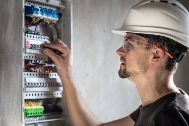 Elektrik santralinde fitillerle çalışan bir elektrik teknisyeni. Elektrik ekipmanlarının kurulumu ve bağlantısı.