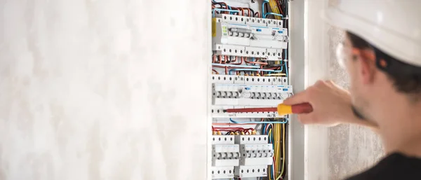 Hombre, un técnico eléctrico trabajando en una centralita con fusibles. Instalación y conexión de material eléctrico . — Foto de Stock