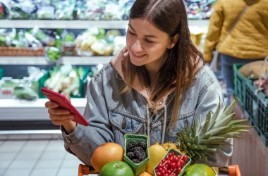Genç bir kadın süpermarketten içinde telefon olan sebzeler alıyor.