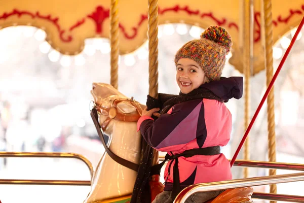 Ein kleines Mädchen fährt auf einem Karussell, Winterurlaub. — Stockfoto