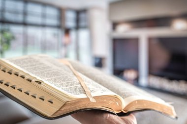 A man holds a Bible against the background of the living room. R