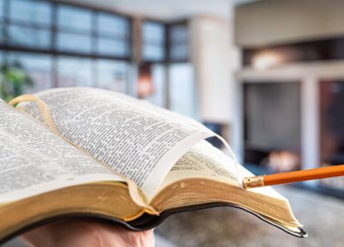A man holds a Bible with a pencil, against the background of the