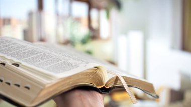 A man holds a Bible and reads a book on the terrace. Morning tim