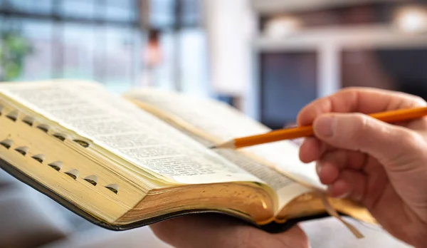 A man holds a Bible against the background of the living room. R — Stok fotoğraf