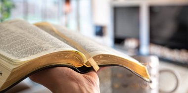 A man holds a Bible against the background of the living room. R