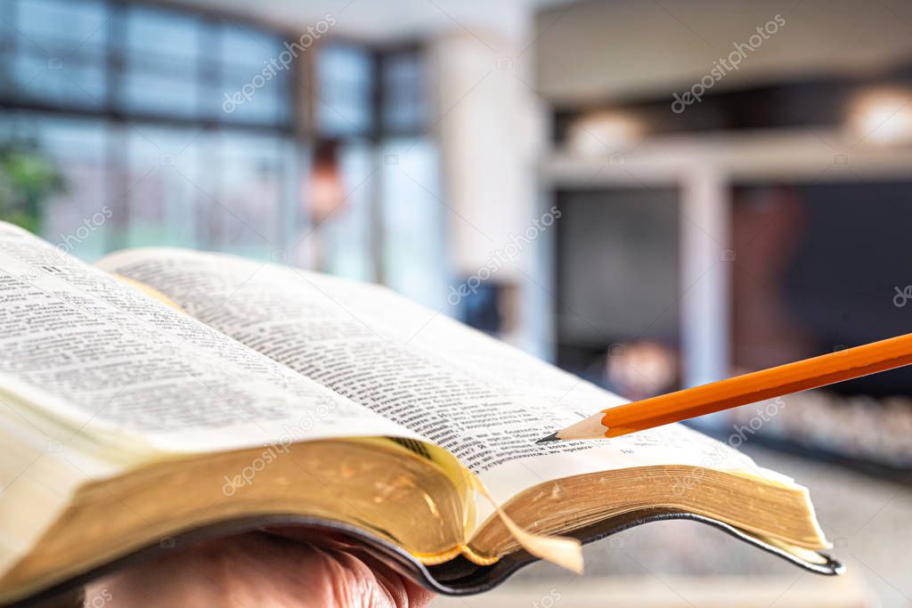 A man holds a Bible with a pencil, against the background of the