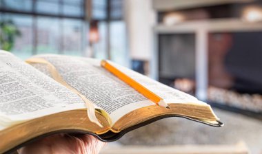 A man holds a Bible with a pencil, against the background of the