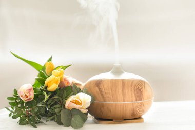 Aroma yağı yayıcı lambası masanın üstünde bulanık bir zemin üzerinde güzel bir bahar lalesi buketi ile.