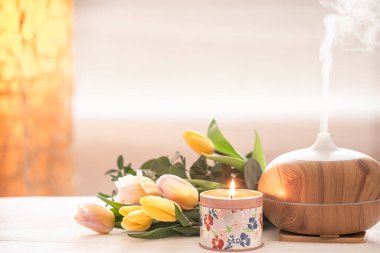 Aromatik yağ yayıcı lambası masanın üzerinde bulanık bir zemin üzerinde güzel bir bahar lalesi buketi ve yanan mumlarla. .