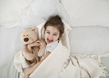 Sevimli küçük bir kız oyuncak bir ayıyla yatakta uyuyor. Çocuk gelişimi ve uyku kavramı. Yukarıdan görünüşü.