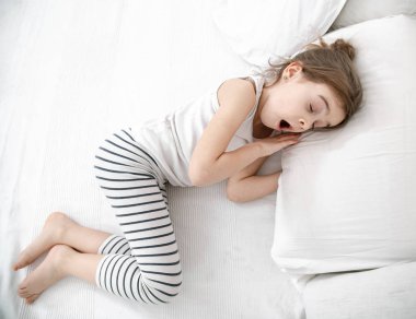 Küçük tatlı bir kız beyaz bir yatakta uyuyor. Çocuk gelişimi ve uyku kavramı. Yukarıdan görünüşü.