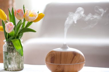 Aroma yağı yayıcı lambası masanın üstünde bulanık bir zemin üzerinde güzel bir bahar lalesi buketi ile.