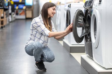 Mağazadaki genç bir kadın çamaşır makinesini seçiyor. Alışveriş konsepti.