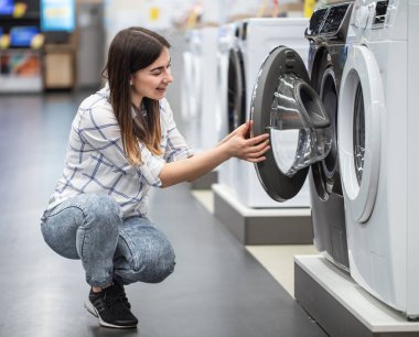 Mağazadaki genç bir kadın çamaşır makinesini seçiyor. Alışveriş konsepti.