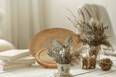 Odanın iç kısmında dekoratif eşyalar, açık ahşap bir masada kurumuş çiçeklerle dolu bir vazo..