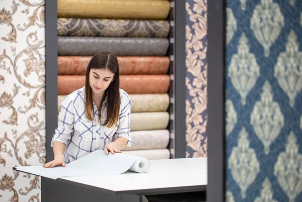 A young woman in a store chooses Wallpaper for her home. Concept of repair and shopping.