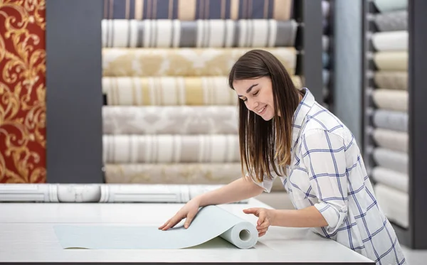 A young woman in a store chooses Wallpaper for her home. Concept of repair and shopping.