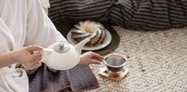 Hands of a young woman pour tea from a teapot. Preparing Breakfast in a cozy home atmosphere.