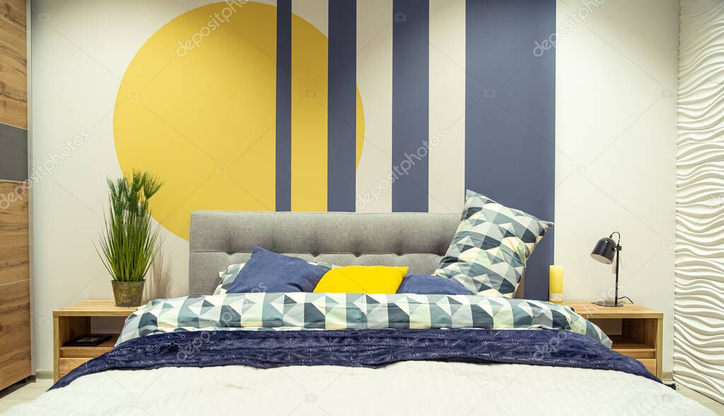 Modern bedroom interior in blue and yellow tones. Large bed with pillows, cozy interior details.