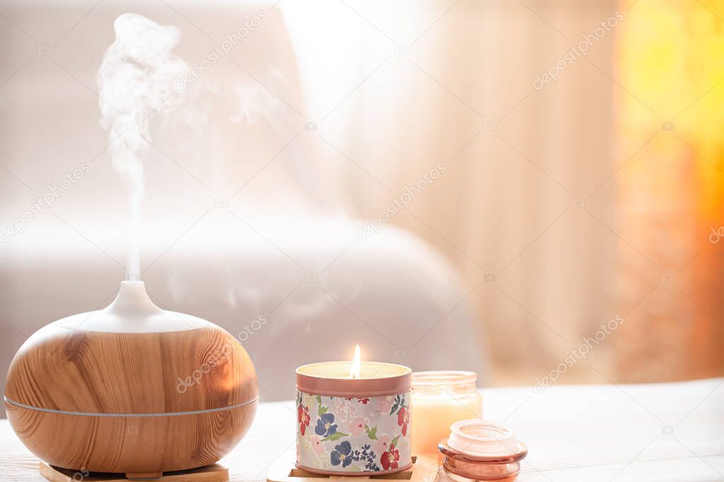 Modern oil aroma diffuser in the living room on the table with burning candles . The concept of refreshing and purifying the air in the house.