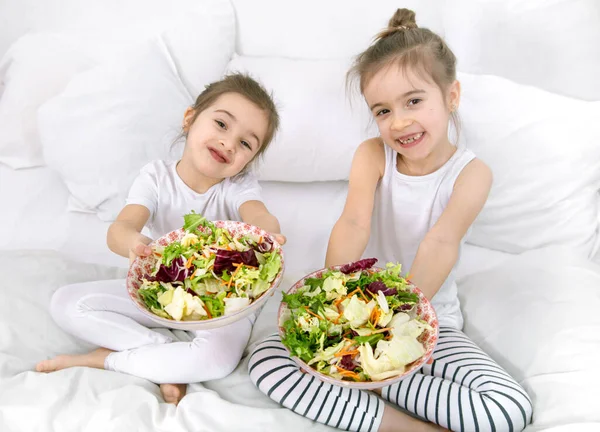 Healthy food at home. Happy two cute children eating fruits and vegetables in the bedroom on the bed. Healthy food for children and teenagers.