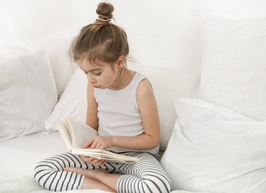 Yatak odasındaki yatakta kitap okuyan tatlı küçük kız. Eğitim ve aile değerleri kavramı .