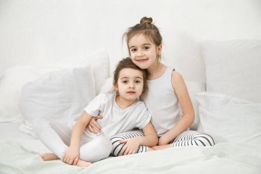 İki küçük kız kardeş yatak odasındaki yatakta sarılıyorlar. Aile değerleri ve çocukların arkadaşlığı kavramı..