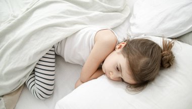 Küçük tatlı bir kız beyaz bir yatakta uyuyor. Çocuk gelişimi ve uyku kavramı. Yukarıdan görünüşü.