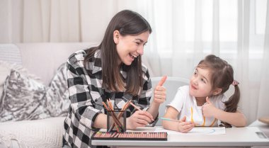 Çocuklu bir anne masada oturur ve ödev yapar. Çocuk evde öğreniyor. Evde eğitim. Metin için boşluk.
