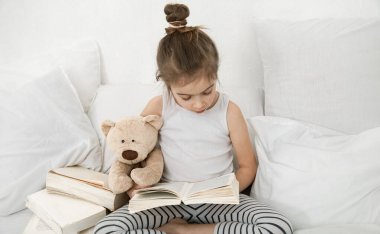 Yatak odasındaki yatakta kitap okuyan tatlı küçük kız. Eğitim ve aile değerleri kavramı .