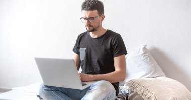 Genç bir adam evdeki bir bilgisayarın başında uzaktan çalışıyor. Serbest Çalışan ve İnternette Çalışan.