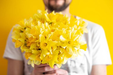 Sarı arka planda, gömlekli bir hippi ve büyük bir buket nergis çiçeği. Selamlama ve kadınlar günü kavramı..